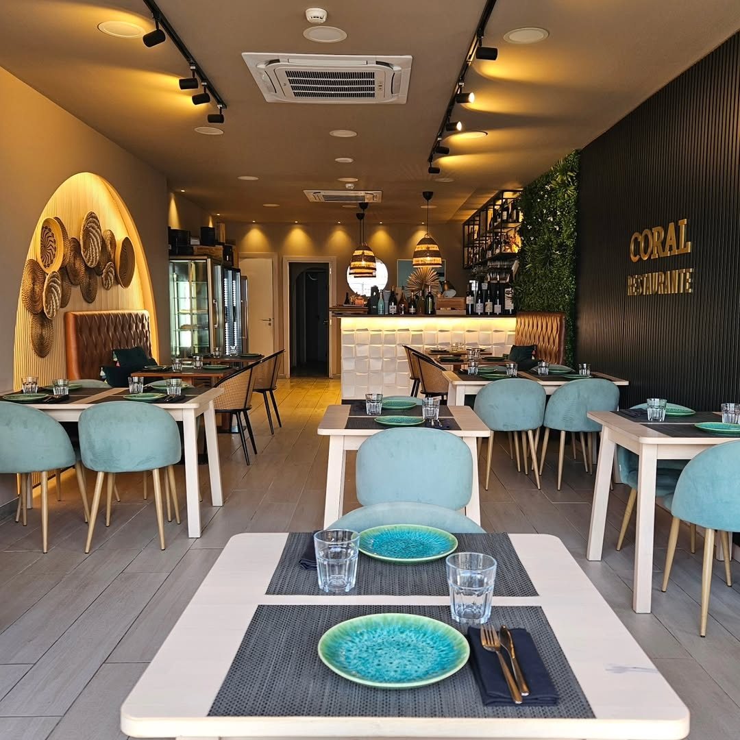 Sala do Coral com mesas postas, cadeiras em verde-água, parede em ripado escuro com o nome do restaurante e balcão ao fundo
