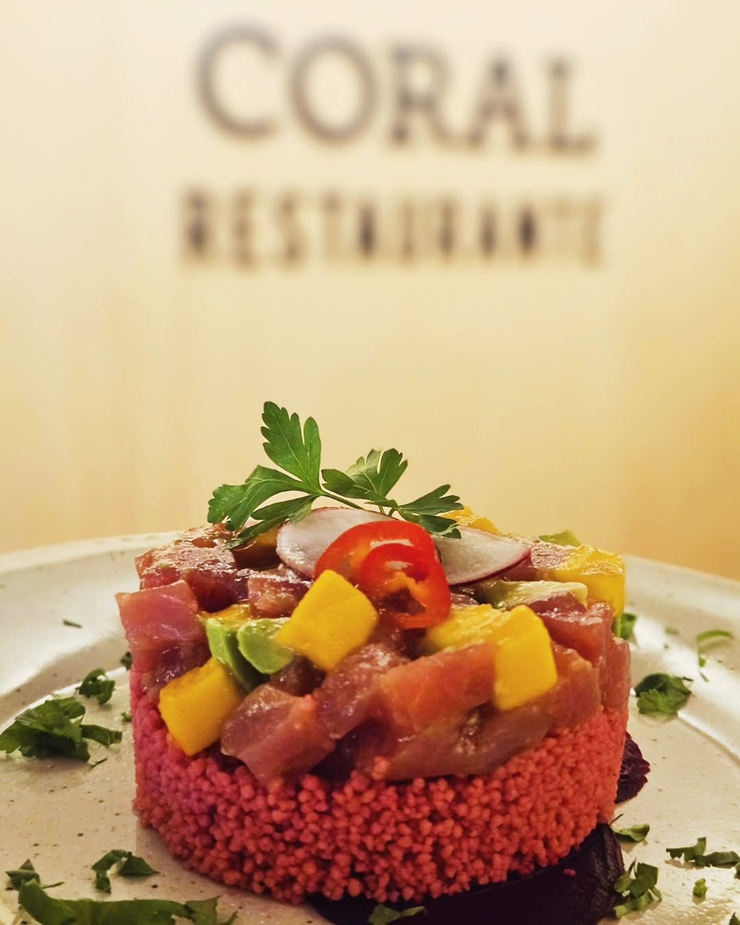 Torre de atum cru com manga e malagueta sobre um leito vermelho, decorada com ervas