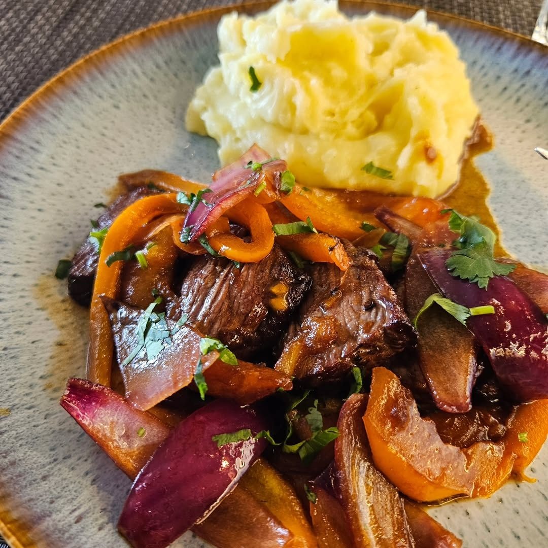 Prato de carne estufada com cebola roxa, pimento e puré de batata